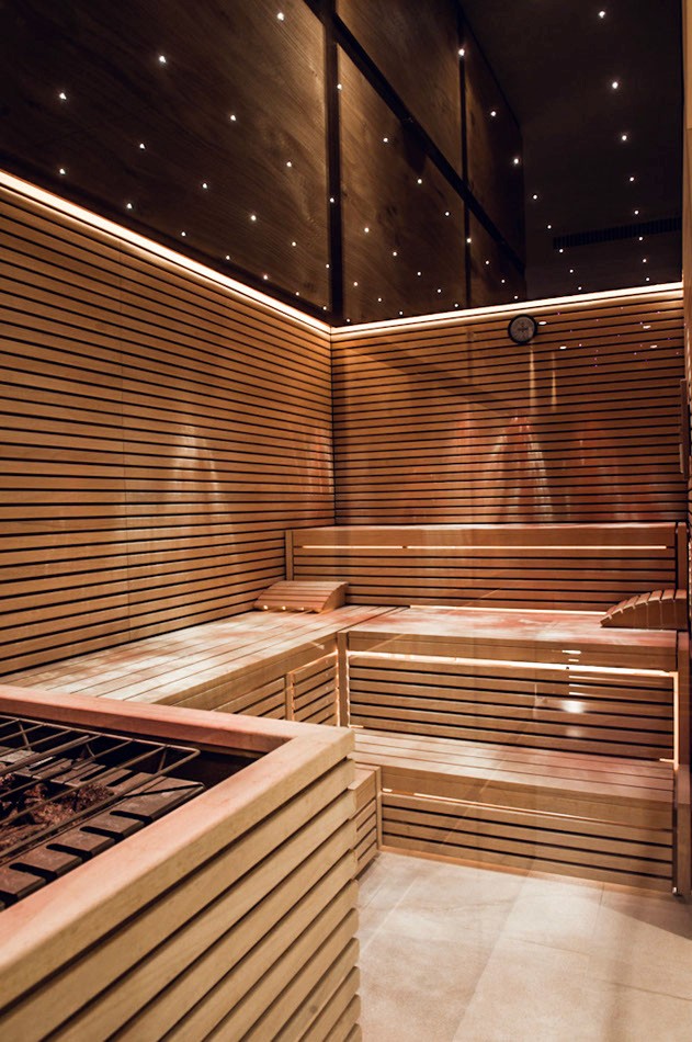 Bio-Sauna hinter Glas, davor runde Naturfaserteppiche auf hellem Stein.
