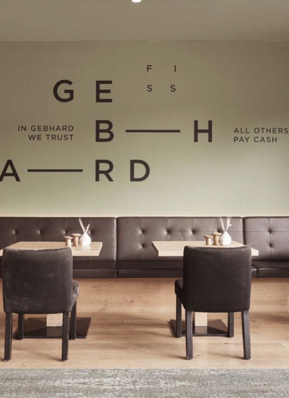 Wandschriftzug GEBHARD über einer braunen Lederbank mit gedeckten Tischen.