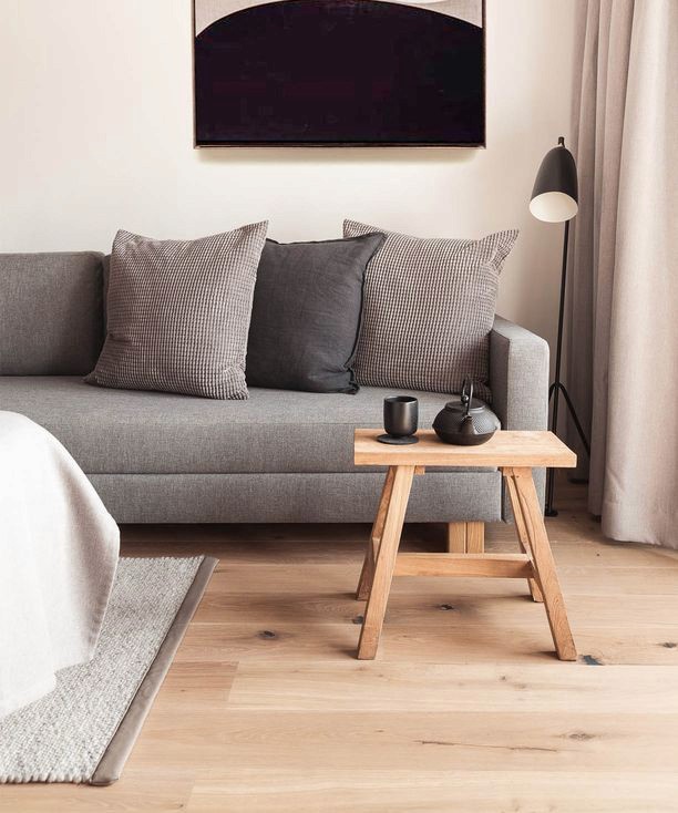 Sitzecke mit grauem Sofa, gemusterten Kissen und kleinem Beistelltisch aus Holz.