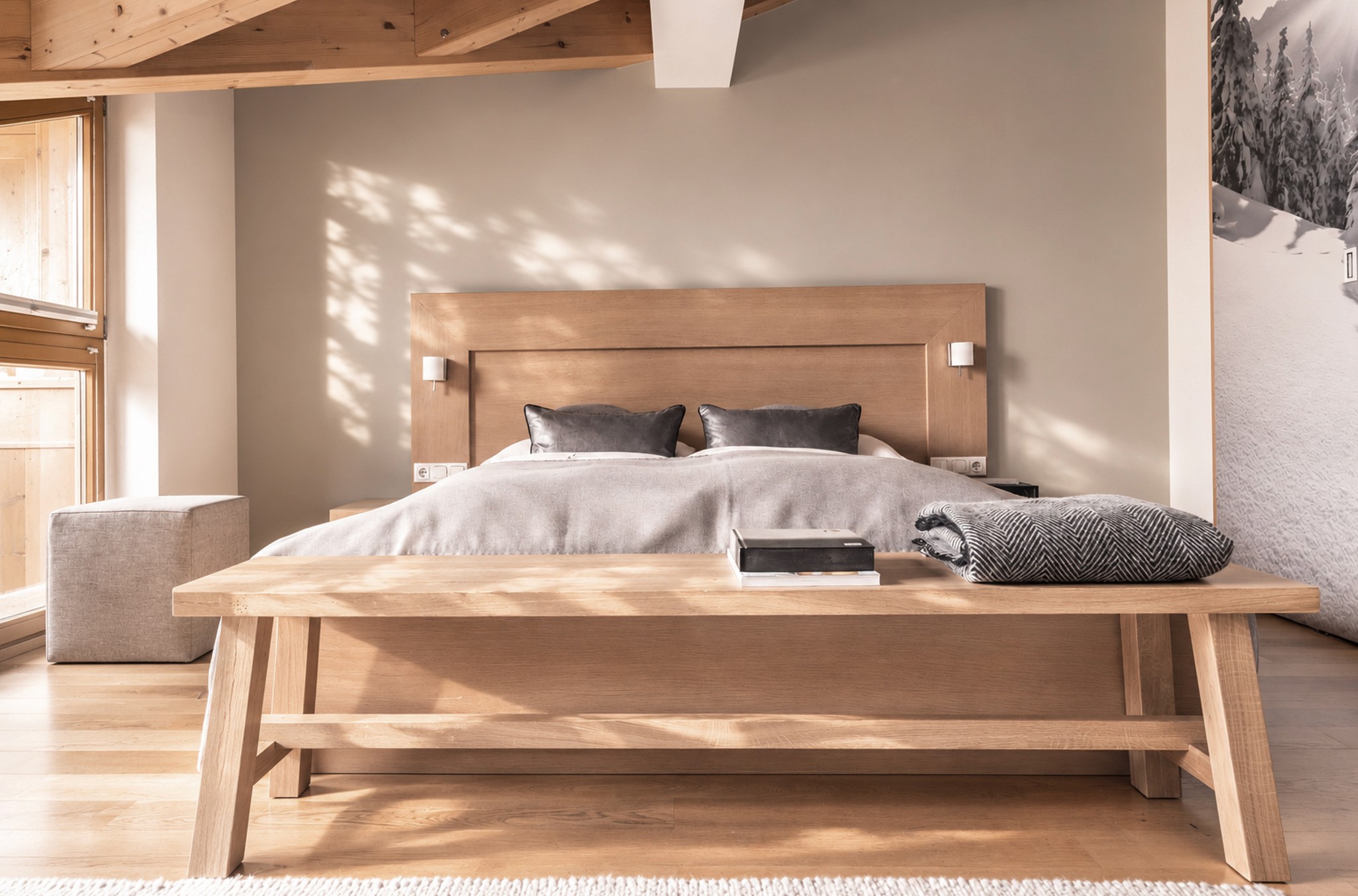 Helles Hotelzimmer mit Holzbett, Sitzbank und Sonnenlicht am Fenster.